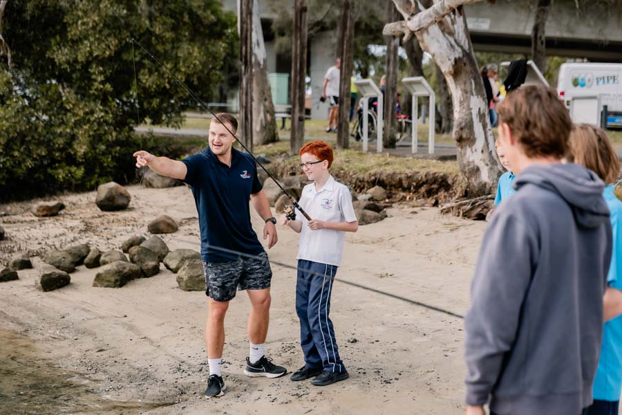 Staff members assisting students in finding a suitable fishing spot, fostering outdoor exploration and learning.